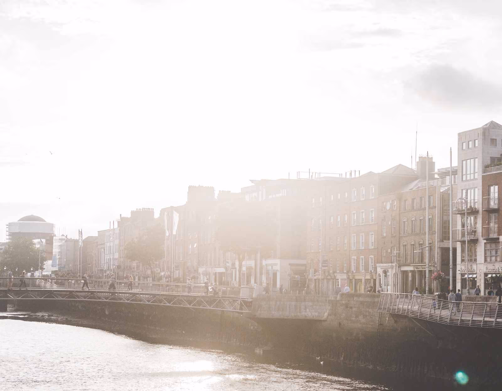 Dublin's River Liffey quays at golden hour, a footbridge crossing the water past the Georgian buildings of the city centre